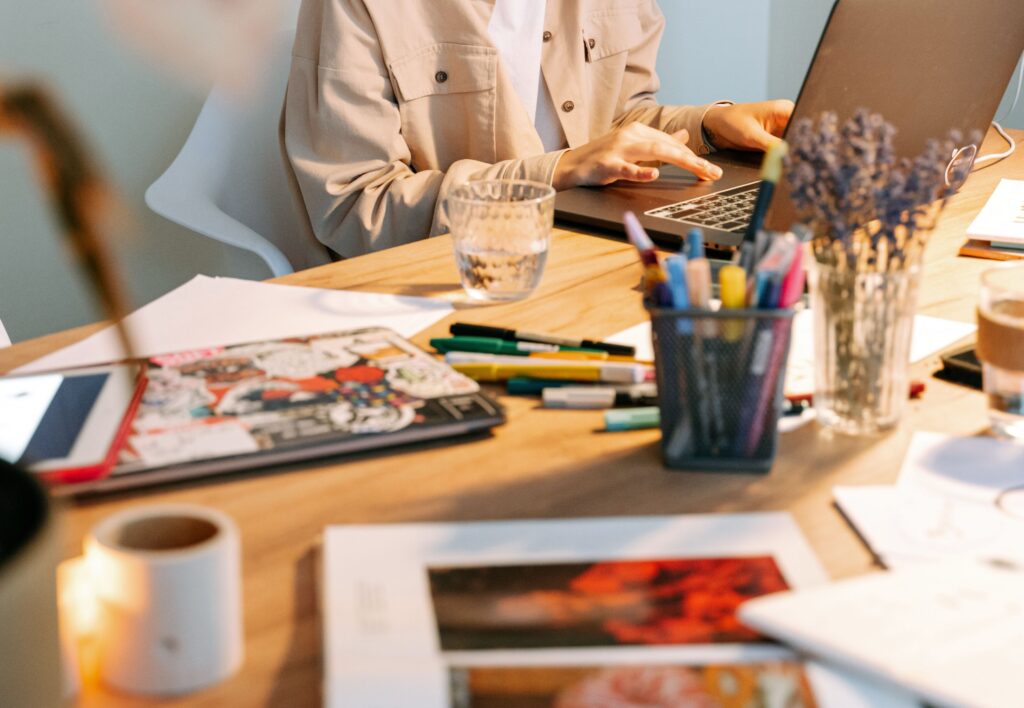 materiales de arte sobre escritorio y diseñadora al fondo en su computadora